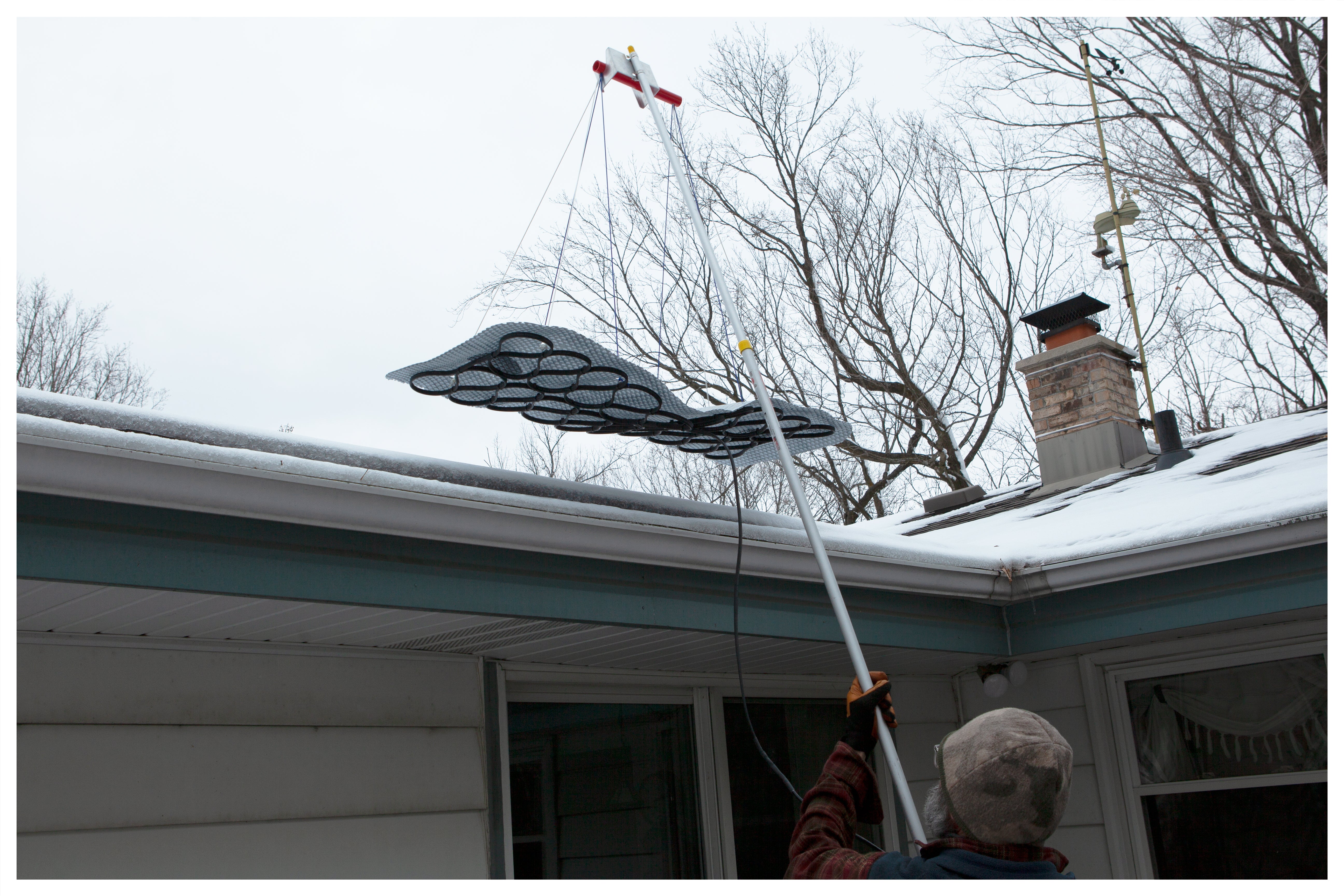 Homeowner placing The Ice Dam Remover on roof using an extension pole with the provided pole mount.